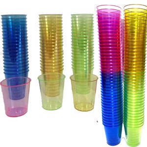 Op de afbeelding: Een stapel van 20 heldere plastic shotglazen in blauw, groen, geel en roze. De glazen zijn gestapeld in vier aparte stapels.