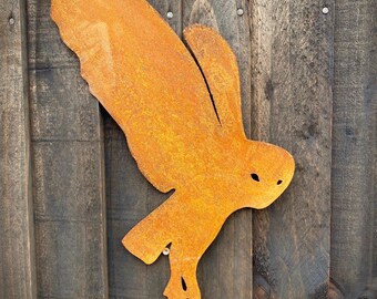 May include: A rusty orange metal owl silhouette mounted on a wooden wall. The owl is in flight with its wings spread out.