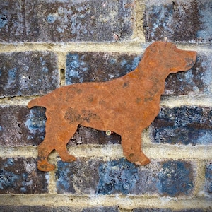Könnte beinhalten: Eine rostige Metallsilhouette eines Hundes, möglicherweise ein Spaniel, an einer Backsteinmauer befestigt.