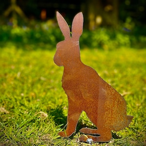 Puede incluir: Una silueta de metal oxidado de un conejo sentado en un campo de hierba.