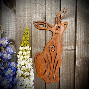 Puede incluir: Una escultura de metal oxidado de un conejo, con un diseño caprichoso, montada sobre una superficie de madera.