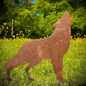 May include: A rusty metal wolf silhouette sculpture stands in a field of yellow wildflowers. The sculpture is facing to the right and has its head tilted up, as if howling.