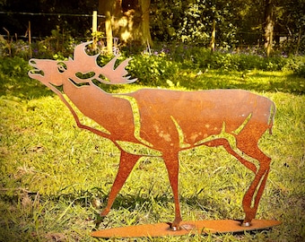 Puede incluir: Una escultura de metal oxidado de un ciervo de pie en un campo de hierba. El ciervo está mirando hacia la derecha y tiene la cabeza inclinada hacia arriba. La escultura está hecha de metal delgado y tiene un aspecto rústico y desgastado.