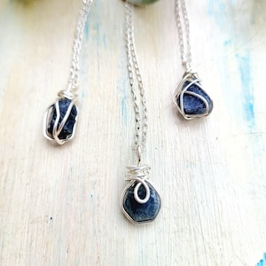 May include: Three silver necklaces with blue gemstone pendants wrapped in silver wire. The gemstones are different shapes and sizes.