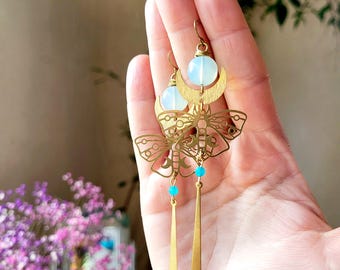 Puede incluir: Pendientes de tono dorado con un diseño de media luna y un dije de mariposa. Los pendientes presentan una piedra de ópalo blanco y cuentas turquesas.