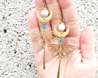Puede incluir: Pendientes de tono dorado con un diseño de media luna, cuentas de perlas blancas y un dije de mariposa detallado. Los pendientes tienen un acento de piedra turquesa.