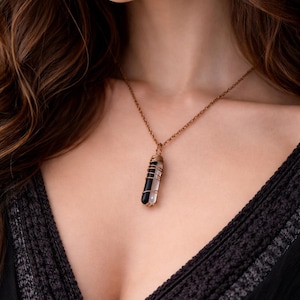 Op de afbeelding: Een ketting met een koperkleurige ketting en een hanger. De hanger heeft een zwarte en heldere kristal, gewikkeld in koperdraad. De ketting wordt gedragen met een zwarte top.