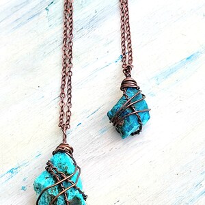 May include: Two turquoise gemstone pendants wrapped in copper wire, hanging from copper chains. The pendants are different sizes and shapes.