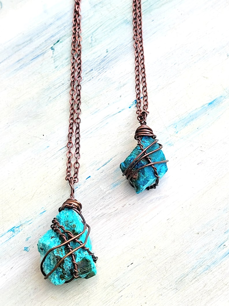 May include: Two turquoise gemstone pendants wrapped in copper wire, hanging from copper chains. The pendants are different sizes and shapes.