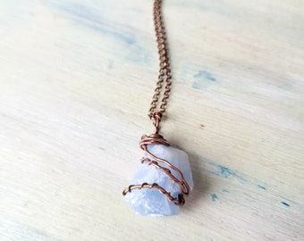 May include: A light blue crystal pendant wrapped in copper wire, hanging from a copper chain necklace. The pendant is a natural, rough-cut stone with a cloudy, translucent appearance.