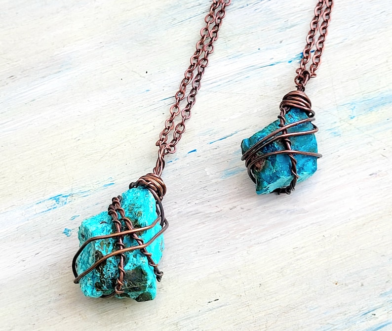 May include: Two turquoise gemstone pendants wrapped in copper wire, hanging from copper chains. The pendants are different sizes and shapes.