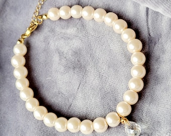 Può includere: Una collana di perle bianche con una catena dorata e un ciondolo a forma di stella. La collana ha un ciondolo di cristallo.