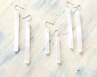 Puede incluir: Un conjunto de cuatro pares de pendientes de cristal de selenita blanca. Los pendientes están hechos de cristales de selenita naturales que se han pulido hasta obtener un acabado liso. Los cristales están suspendidos de alambres para orejas plateados.