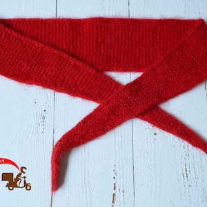 May include: A vibrant red knitted headband, displayed on a white wooden surface. The headband is made of a soft, textured material and is designed to be worn around the head. The ends are crossed over each other.