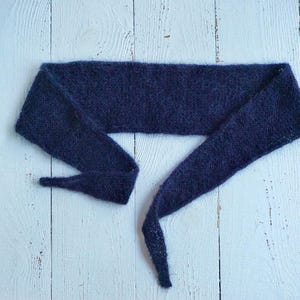 Op de afbeelding: Een lange, donkerblauwe gebreide sjaal met een puntig uiteinde. De sjaal is gemaakt van zacht, pluizig garen.