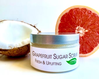 May include: A jar of grapefruit sugar scrub with a silver lid, labeled "Grapefruit Sugar Scrub Fresh & Uplifting." A halved grapefruit and a piece of coconut are in the background. The jar contains 4 oz / 113 g of product.