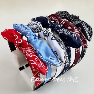 May include: Set of six colorful headbands with bandana-style fabric bows. The headbands are black and the bows are red, blue, white, and two shades of blue. The headbands are displayed on a white stand with the text "BRIGHT IDEAS NYC".