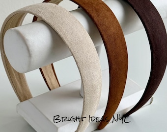 Puede incluir: Tres diademas con una textura suave similar al ante en color crema, marrón claro y marrón oscuro. Las diademas se muestran en un soporte cilíndrico blanco. El texto BRIGHT IDEAS NYC está impreso en negro en la base del soporte.
