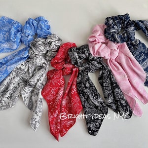May include: Set of six colorful hair scrunchies with bandana-style fabric. The scrunchies are in blue, white, red, black, and pink with a paisley pattern.