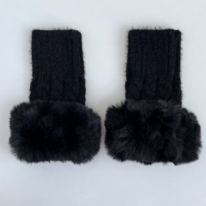 May include: A pair of black knitted leg warmers with a fluffy black faux fur trim.