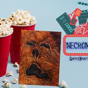 May include: A red and white papercraft movie poster with the title "NECRONOMICON" and the text "PAPERCRAFT MATCHBOX". The poster is surrounded by movie-themed items, including popcorn, a ticket, and 3D glasses.