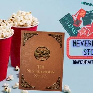 May include: A red and white movie theater ticket, a pair of red and white 3D glasses, a red and black clapperboard, and a red and white popcorn bucket with popcorn spilling out. The background is a blue wall with the words "NEVERENDING STORY" in a red and white marquee. The words "PAPERCRAFT MATCHBOX" are below the marquee.