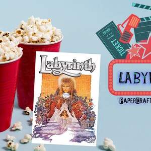 May include: A red and white movie poster for the film Labyrinth, featuring David Bowie as Jareth the Goblin King. The poster is next to two red cups filled with popcorn. The cups are on a light blue background.