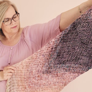 Pode incluir: Uma mulher segura um cachecol de malha rosa e roxo degradê com um padrão texturizado.