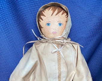 May include: A vintage cloth doll with a white dress, brown hair, and blue eyes. The doll is wearing a bonnet and has a lace trim on the dress.