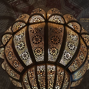 May include: A large, ornate, gold-colored metal Moroccan pendant light fixture with a geometric pattern. The light is on and casting a warm glow.