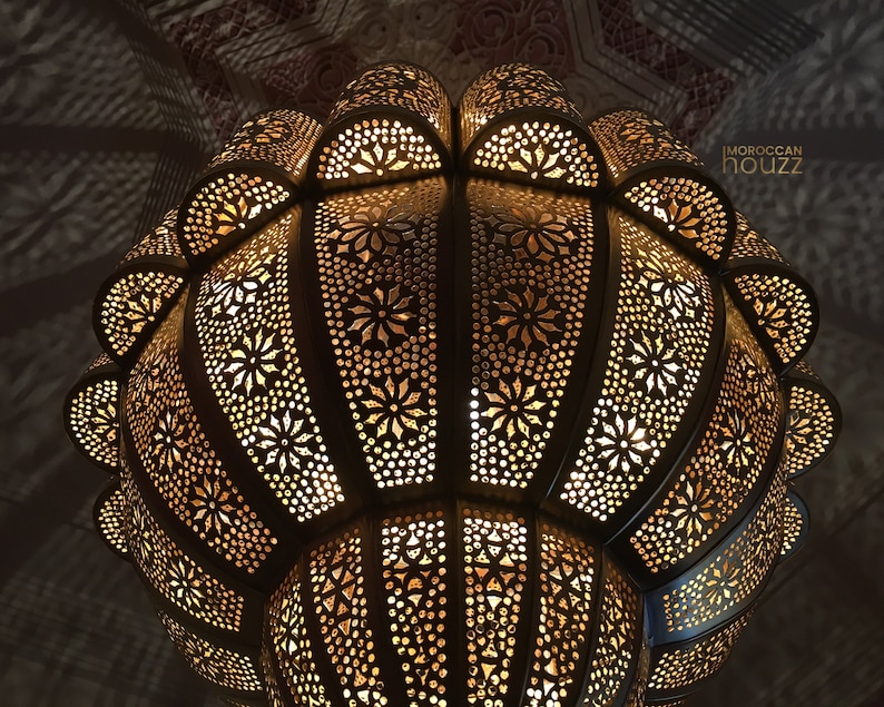 May include: A large, ornate, gold-colored metal Moroccan pendant light fixture with a geometric pattern. The light is on and casting a warm glow.
