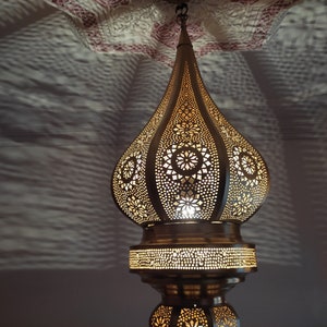 May include: A gold Moroccan pendant light with intricate cut-out designs. The light is hanging from a ceiling and casting a warm glow.