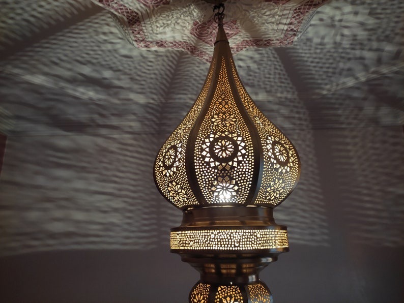 May include: A gold Moroccan pendant light with intricate cut-out designs. The light is hanging from a ceiling and casting a warm glow.