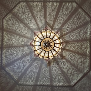 May include: A large, ornate, metal ceiling light fixture with a starburst design. The light fixture casts intricate shadows on the ceiling.