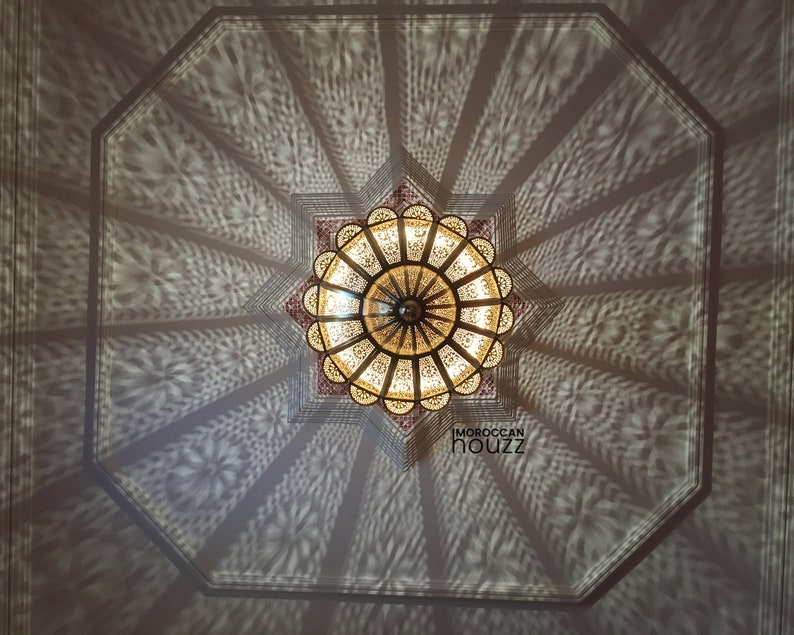 May include: A large, ornate, metal ceiling light fixture with a starburst design. The light fixture casts intricate shadows on the ceiling.