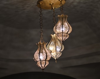 Könnte beinhalten: Verzierte, goldfarbene Pendelleuchten mit aufwendigen Ausschnitten hängen von der Decke. Die Lampen haben eine tulpenartige Form und strahlen ein warmes, einladendes Licht aus. Die Decke ist dunkelgrau.