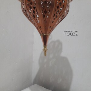 May include: A copper Moroccan lantern with intricate cut-out designs. The lantern is hanging from the ceiling and has a pointed tip at the bottom.