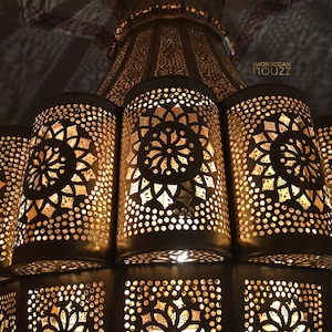 May include: A gold metal Moroccan chandelier with intricate cut-out designs. The chandelier has a round top and multiple tiers of lights.