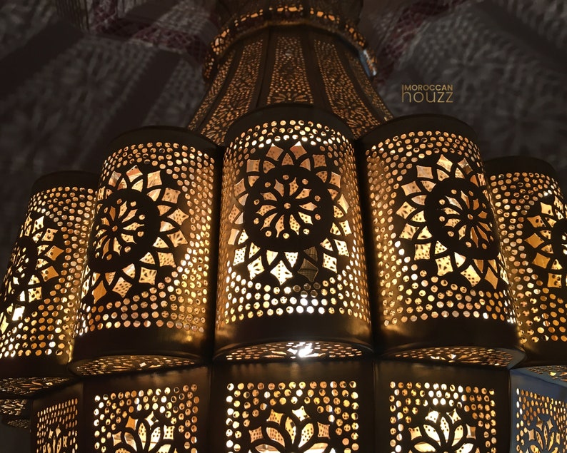 May include: A gold metal Moroccan chandelier with intricate cut-out designs. The chandelier has a round top and multiple tiers of lights.