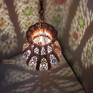 May include: A Moroccan-style hanging lantern with intricate metalwork and colorful glass accents. The lantern casts a warm glow and creates beautiful shadows on the ceiling.