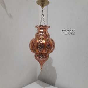 May include: A copper Moroccan pendant light with intricate cutouts and colorful glass accents. The light is hanging from a chain and has a traditional design.