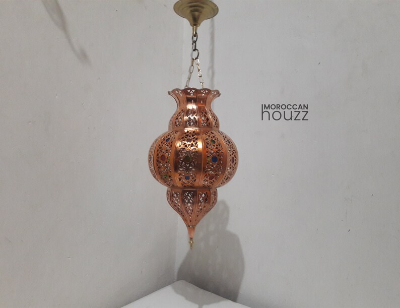 May include: A copper Moroccan pendant light with intricate cutouts and colorful glass accents. The light is hanging from a chain and has a traditional design.