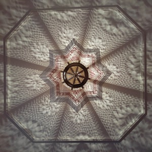May include: A star-shaped ceiling light fixture with a geometric pattern casts a shadow on a white ceiling. The light fixture is made of metal and has a brown finish.