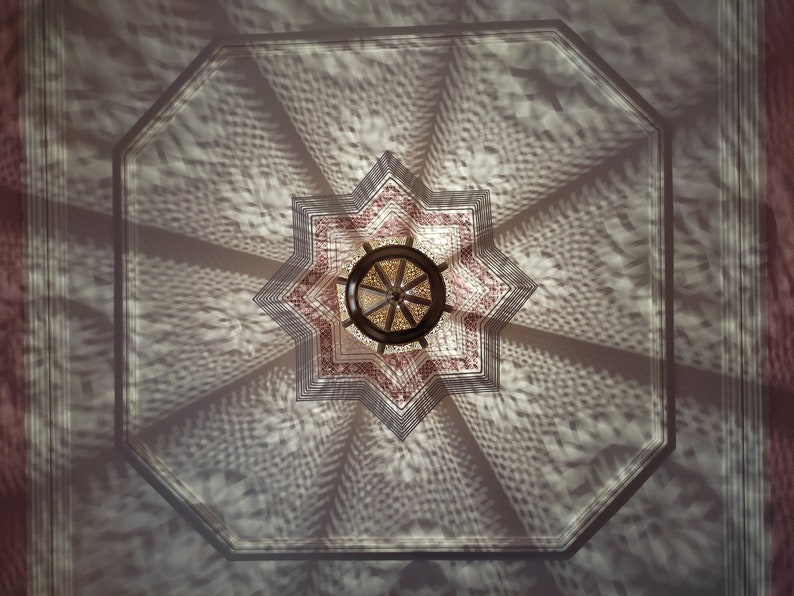 May include: A star-shaped ceiling light fixture with a geometric pattern casts a shadow on a white ceiling. The light fixture is made of metal and has a brown finish.