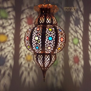 May include: A Moroccan lantern with intricate metalwork and colorful glass accents. The lantern is hanging from the ceiling and casting a decorative shadow on the wall.