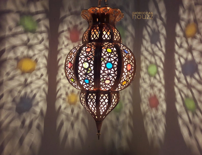 May include: A Moroccan lantern with intricate metalwork and colorful glass accents. The lantern is hanging from the ceiling and casting a decorative shadow on the wall.