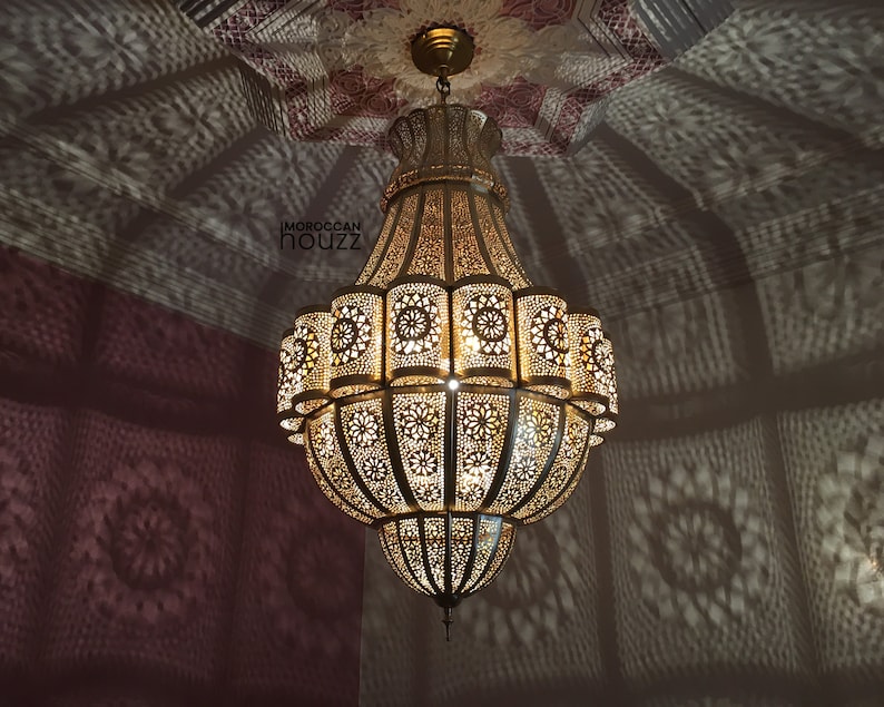 May include: A large, ornate gold chandelier with intricate cut-out designs. The chandelier has a round, bell-shaped design and hangs from a chain.
