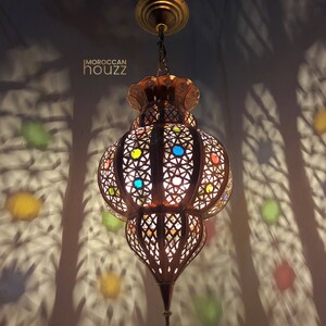 May include: A Moroccan-style pendant light fixture with a round, ornate metal frame and colorful glass accents. The light casts intricate shadows on the wall.