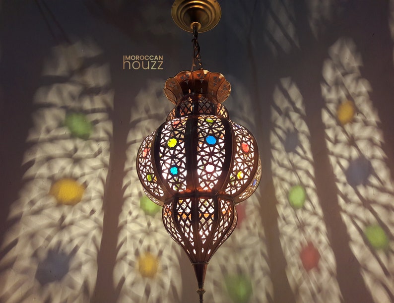 May include: A Moroccan-style pendant light fixture with a round, ornate metal frame and colorful glass accents. The light casts intricate shadows on the wall.