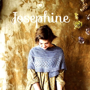 May include: A blue and white crocheted shawl with a lacy pattern. The shawl is worn by a person with brown hair and is draped over a yellow shirt. The background is a textured brown surface with the text "LONDON LOOP Josephine" in white.